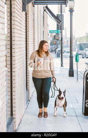 Eine weibliche Latina Spaziergänge mit ihrem Hund während Kaffee trinken in der Stadt Stockfoto