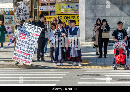 Eine Person mit Plakaten Stufen eine ein Mann protestieren, die als Touristen in traditionelle koreanische Kleidung warten gekleidet die Straße an einem fußgängerüberweg zu überqueren. Stockfoto