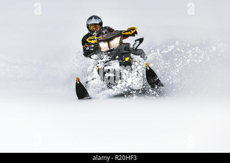 In tiefe Schneeverwehungen snowmobile Fahrer schnell in die Kurve fahren. Reiten mit Spaß in tiefem Schnee Pulver während der backcountry Tour. Extreme Sport Outdoor Abenteuer. Stockfoto