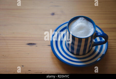 Babyccino in einem blau-weiß gestreiften Espresso Tasse und Untertasse auf einem Holztisch Stockfoto