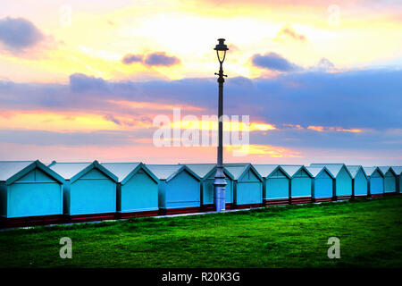 Brighton Seafront eine Linie dreizehn Badekabinen, mit einem viktorianischen Straßenlaternen in der Mitte die Sonne und der Himmel leuchtet gelb, rot, und/oder Stockfoto