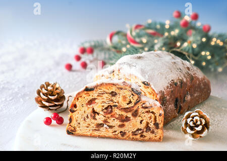Christstollen auf Weiß-Blau festliche Hintergrund mit Tannen Zweigen, Zapfen und Beeren. Traditionelle deutsche Dessert für Weihnachten feiern. Stockfoto