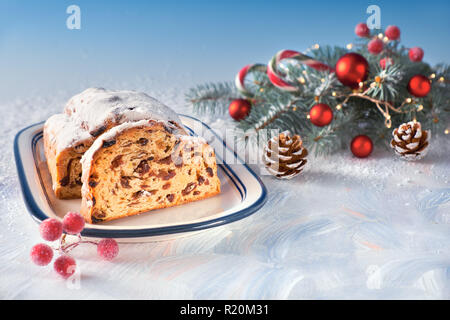 Christstollen auf Weiß-Blau festliche Hintergrund mit Tannen Zweigen und Nippes. Traditionelle deutsche Dessert für Weihnachtsfeier, Bild horizontal Stockfoto