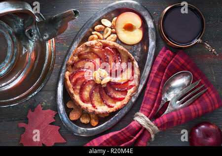 Hausgemachte pflaume Torte serviert mit Erdnüssen auf hölzernen Tisch. Ansicht von oben mit Geschirr, schwarzer Tee und Kupferkessel auf dunklen Holz. Stockfoto