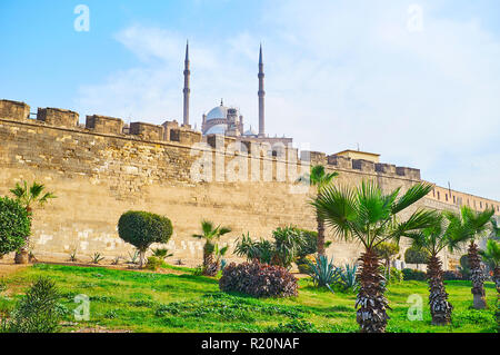 Die malerischen, grünen Garten mit Palmen, Bäumen und Blumenbeeten vor der mittelalterlichen Mauer der Zitadelle von Saladin, Ausblenden der malerischen Alabaster Moschee Stockfoto