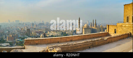 Der Blick von der äußeren Mauer der Zitadelle von Saladin auf dem Islamischen Kairo mit hazy Wohnquartiere, Al Rifai und Sultan Hassan Moschee am Sunset, z. B. Stockfoto