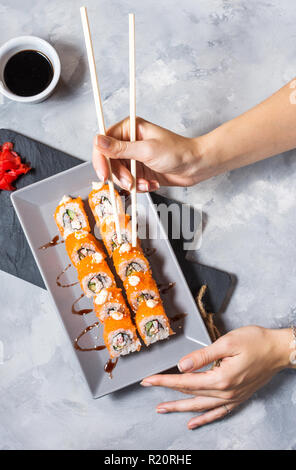 Hand mit Stäbchen auf Sushi mit Sojasauce auf konkrete Tabelle einrichten. Ansicht von oben Stockfoto