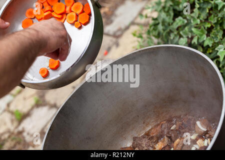 Hinzufügen von Karotte in einen Kessel mit Lamm. Vorbereitung der Chorba Suppe auf offenem Feuer, traditionelle Mahlzeit für viele nationale Spezialitäten, die in Europa, Afrika und Asien Stockfoto