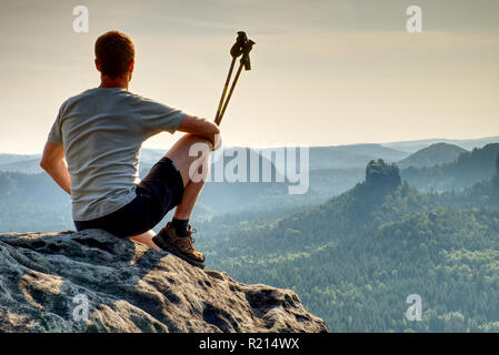 Wanderer in trekking Kleidung sitzen allein auf Rock Gipfel. Wundervoller Sonnenaufgang in den Bergen Stockfoto