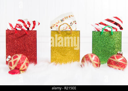 Drei prickelnde Geschenk Taschen in einer Reihe auf einem weißen Hintergrund und Fell mit rot und gold Weihnachtsornamente Stockfoto