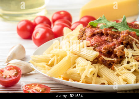 Italienische Pasta Bolognese Penne rigatone Hackfleisch in Tomatensoße und Parmesan. Noch immer leben auf weiße Holztisch mit Cherry Tomaten serviert, Karaffe Olivenöl und Glas Weißwein Stockfoto