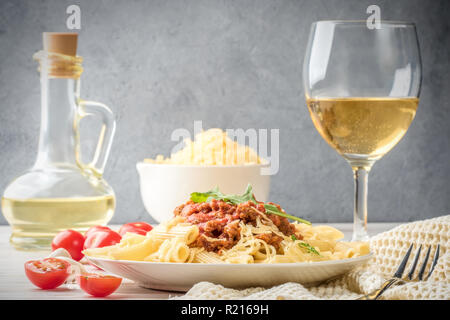 Italienische Pasta Bolognese Penne rigatone Hackfleisch in Tomatensoße und Parmesan. Noch immer leben auf weiße Holztisch mit Cherry Tomaten serviert, Karaffe Olivenöl und Glas Weißwein Stockfoto