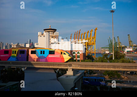 Eine Sentosa Express Zug, Singapur, weg von VivoCity Mall zur Sentosa Insel; b/g: Veranstaltungsort St. James Power Station und dem Hafen Stockfoto