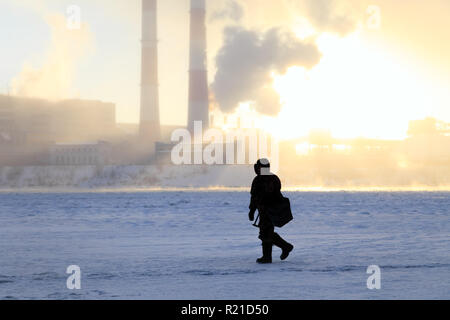 Winter angeln, Leidenschaft, Fischer fangen Fische auf einem zugefrorenen Fluss vor dem Hintergrund der Fabrik Rohre bei Sonnenuntergang. Konzept von Öl und Gas pr Stockfoto