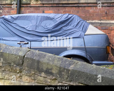 Ein blauer VW Golf MK2 Cabrio Limousine Auto mit einer Abdeckung über es, neben einem alten heruntergekommenen Haus in Durham City, County Durham, England, UK geparkt Stockfoto