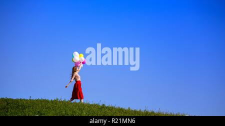 Happy girl In den Wiesen der Toskana mit bunten Luftballons, gegen den blauen Himmel und grüne Wiese. Toskana, Italien Stockfoto