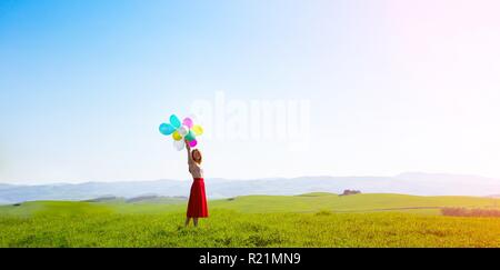 Happy girl In den Wiesen der Toskana mit bunten Luftballons, gegen den blauen Himmel und grüne Wiese. Toskana, Italien Stockfoto