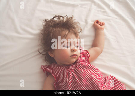 Baby Mädchen Schlafen auf dem Rücken mit offenen Armen und ohne Schnuller in einem Bett mit weißer Bettwäsche. Ruhigen Schlaf in einem hellen Raum. Pastellfarben retro getönt. Sof Stockfoto