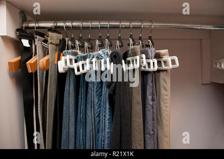 Jeans und Hosen auf Kleiderbügeln hängen in einer Reihe in den Schrank, gut organisiert Stockfoto