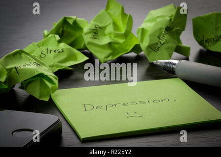 Depression. Das Wort 'depression' auf grünen Zettel auf Holz- schwarz Tabelle geschrieben wird. Zerknitterte grün Haftnotizen sind verstreut mit Texten Stockfoto