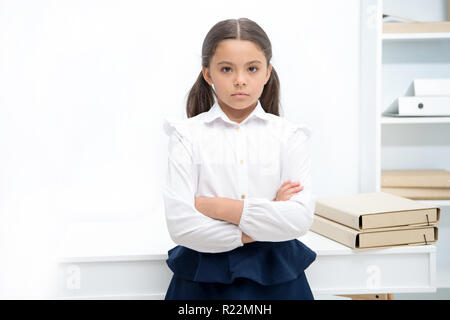 Smart Blick. Kind Mädchen trägt uniform Stehen mit verschränkten Armen auf der Brust. Schulmädchen smart Kind schwerwiegende innen weiß Hintergrund. Mädchen ernst über Wissen und Bildung in der Schule. Stockfoto