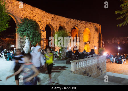 Hama, Hama Governatorat, Syrien: syrischen Familien sitzen in der Nacht an der Open-air-Kaffeehaus durch das alte Aquädukt, der Großen Moschee Witz zu liefern Stockfoto