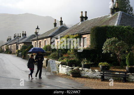 Ein paar Spaziergänge unter einem Sonnenschirm im Regen in Luss, Schottland Stockfoto