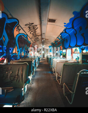 Graffiti bedeckt Zug Auto innen. Grunge Look eines verlassenen Warenkorb mit Sitzplätzen zerschnitten und blau Graffiti an den Wänden und Fenstern. Stockfoto