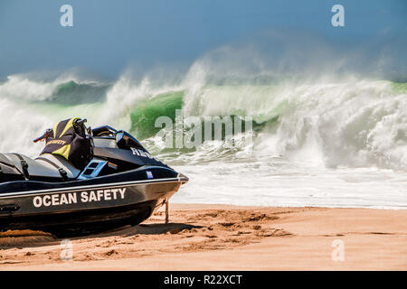 Rettungsschwimmer jetski sitzt auf dem goldenen Sandstrand von Hawaii als Big Wave stürzt im Hintergrund. Stockfoto