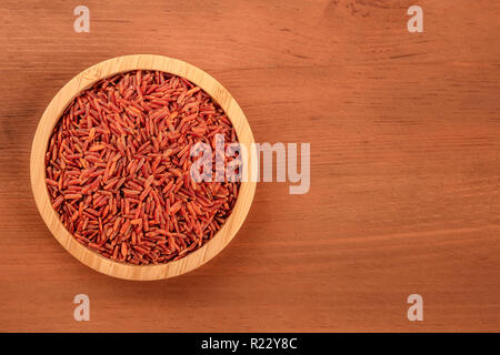 Roter Reis, Schuß von oben in eine hölzerne Schüssel auf einem dunklen Hintergrund im Landhausstil mit einem Platz für Text Stockfoto