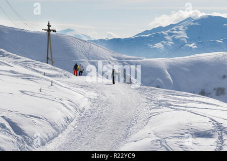 Skifahrer und Snowboarder gehen auf Schnee Straße am sonnigen Morgen. Kaukasus, Georgien, Region Gudauri. Stockfoto