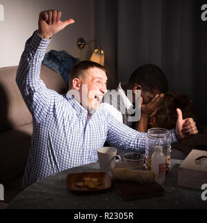 Zwei aufgeregt männlichen interracial Freunde zusammen, Fußball Spiel zu Hause Stockfoto