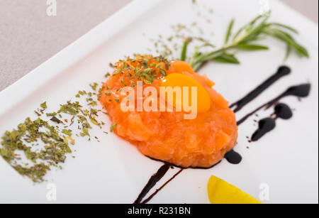 Tartar von frischem Lachs auf weiße Platte. Rezept: fein hacken 200 g Fisch, Würzen sie mit Salz, schwarzem Pfeffer, Olivenöl, Zitronensaft, garniert mit Eigelb Stockfoto