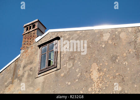 Blick auf das Dach des alten Gebäudes, kaputte Fenster, Dachluke, closeup/Kamin und blauen Himmel im Hintergrund/Dach eines älteren Hauses. Fassade Stockfoto