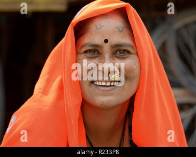 Im mittleren Alter Rajasthani Frau mit traditionellen Nase Schmuck und Tribal Tattoos auf Kinn und Stirn trägt einen orangefarbenen Kopftuch (DUPATTA). Stockfoto