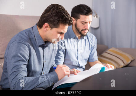 Zwei ernste Männer Arbeiten mit Dokumenten, während auf dem Sofa zu Hause sitzen Stockfoto