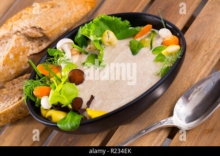 Leckere Cremesuppe mit verschiedenen Pilzen garniert mit geschnittene Karotten, Sellerie und Grüns, serviert mit Brot Stockfoto