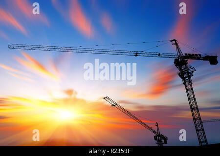 Industriebau-Krane und Gebäude Silhouetten über Sonne bei Sonnenaufgang. Stockfoto