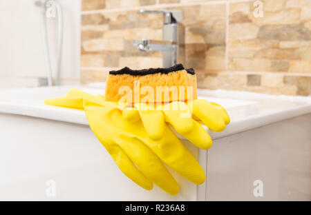 Gelb sanitär Gummihandschuhe und orange Schwamm am Rand der weißen Porzellan Waschbecken Stockfoto