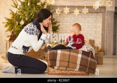 Die Mutter tröstet sie wenig weinenden Sohn auf dem Hintergrund der Weihnachtsbaum und festliche Girlanden. Stockfoto