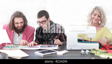 Lächelnd Geschäftsfrau maßgeschneiderte sitzen an der Nähmaschine und handgefertigte Kleidung, während Marketing Assistant arbeiten an neuen Projek Stockfoto