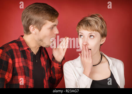 Junger Mann etwas überrascht, Frau zu reden. Studio auf rotem Hintergrund Stockfoto