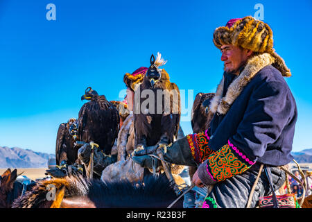 ULGII, Mongolei - OKTOBER 6, 2018: Golden Eagle Festival. Die mongolischen Reiter auf dem Pferd in traditioneller Kleidung mit Adler in der Hand re Stockfoto