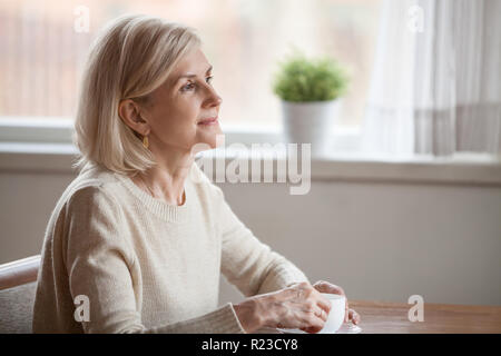 Nachdenklich senior Frau trinkt Kaffee oder Tee etwas zu träumen, verträumte älteren Mädchen Freizeit zu Hause, denken über angenehme memori Stockfoto
