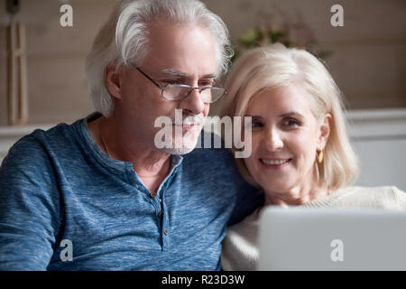 Nahaufnahme von Happy älterer Mann und Frau auf Sofa Video at laptop entspannen, lächelnd im Alter von Paar rest verbringt romantische Zeit an mit Comput home Stockfoto