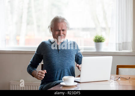 Erschöpft alter Mann leiden unter Rückenschmerzen sitzen zu lange in falsche Körperhaltung, müde älterer männlichen Ausdehnung in Stuhl Arbeiten am Laptop in Körper sp Stockfoto