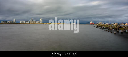 Kormorane sammeln Auf einem heruntergekommenen verlassenen Pier in Edinburghs Leith Docks, mit Apartment Gebäude der westlichen Hafen Stadterneuerung neighbou Stockfoto