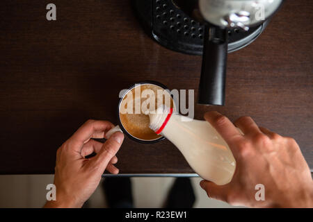 Foto der Kaffeemaschine, die Hände des Menschen gießen Milch in die kaffeetasse Stockfoto