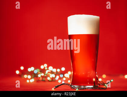 Pint Glas Helle Lagerbier oder Ale mit großen Kopf von Schaumstoff- und Weihnachtsbeleuchtung auf rotem Hintergrund Stockfoto