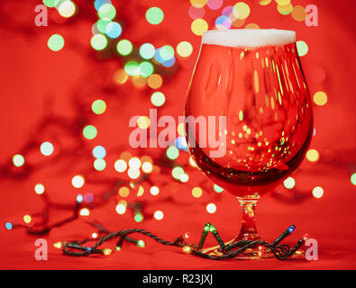 Kurze Glas helles Lagerbier oder Ale mit Weihnachtsbeleuchtung auf rotem Hintergrund Stockfoto